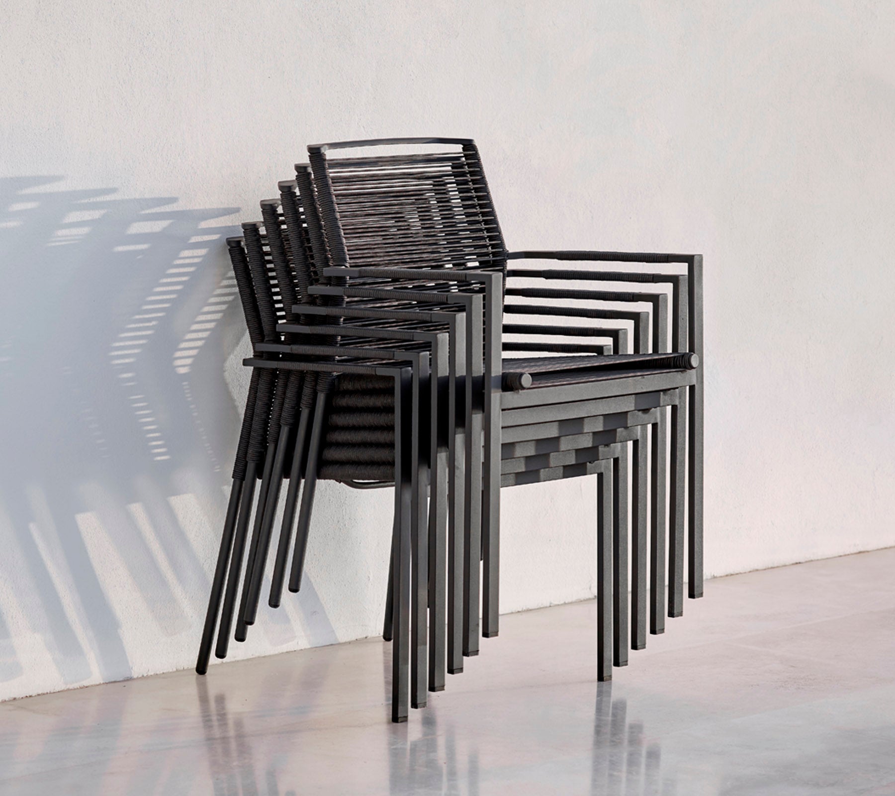 A stack of modern black chairs with a sleek design, casting shadows against a light background.