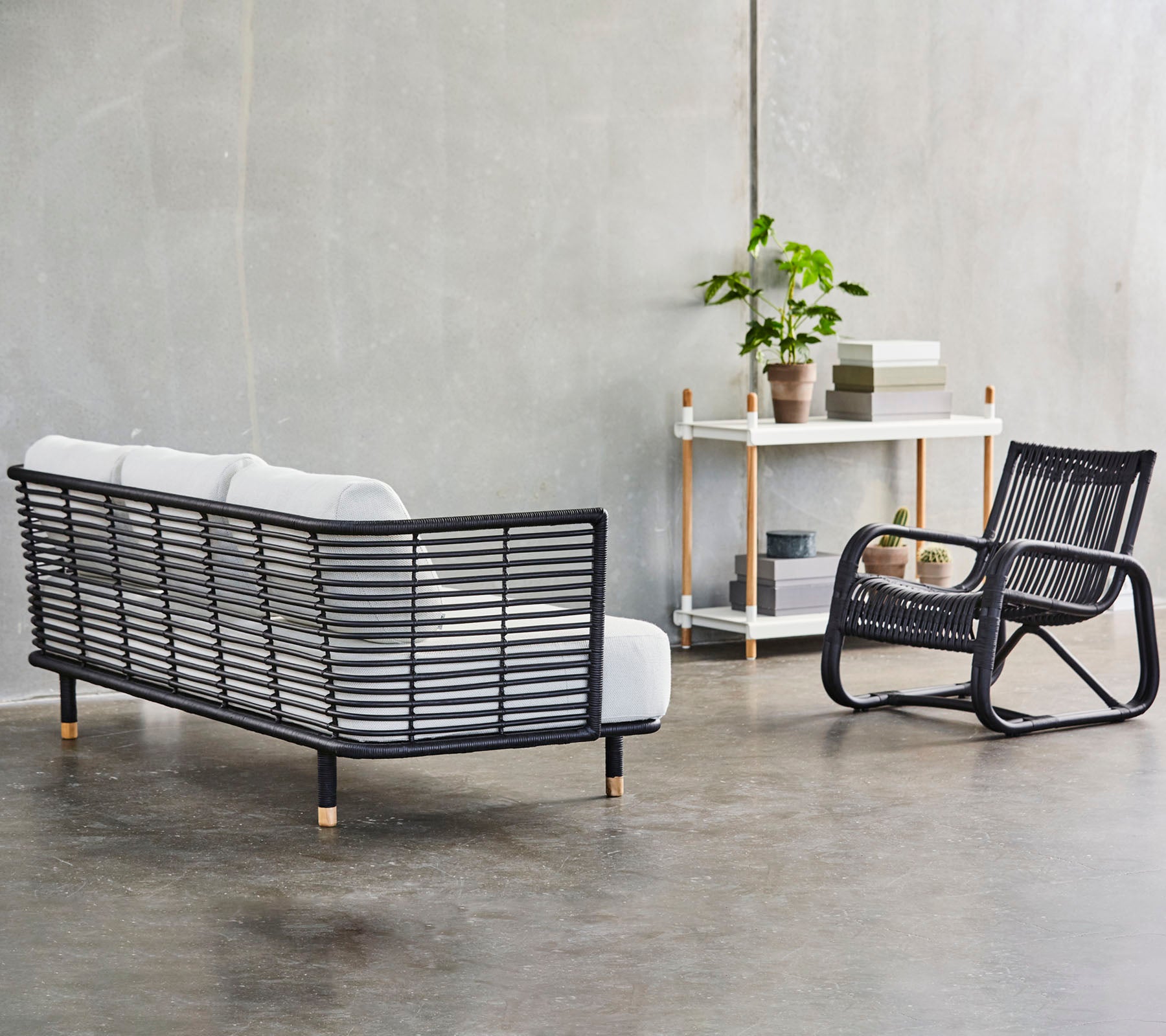 A modern seating arrangement featuring a stylish black frame couch with white cushions and a matching rocking chair, accented by greenery.