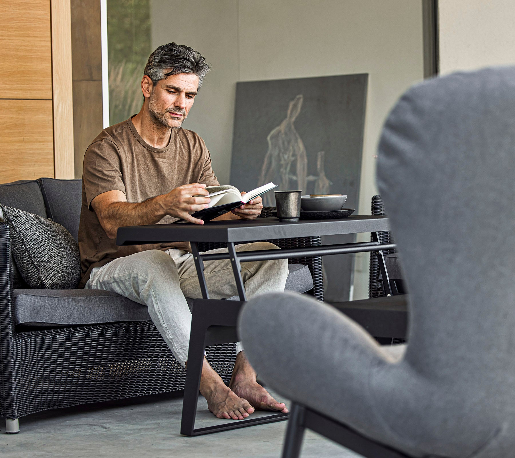 A man sitting on a couch, reading a book with a cup beside him, in a stylish and relaxed setting.