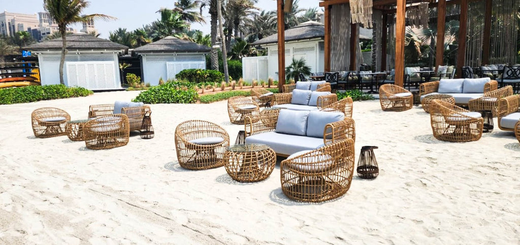 Lounge at the beach furnished with outdoor 2-seater sofas, round lounge chairs and side tables in natural
