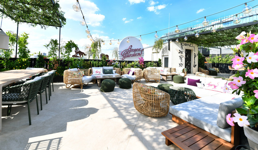 Grace Garden bar and lounge atop of Hotel Zoo Berlin. A sunny day with blue skies, lounge furniture from Cane-line Nest series and green dining chair from Cane-line Ocean series. Green plants and rosa flowers