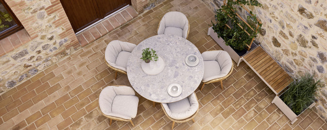A round table surrounded by four cushioned chairs, featuring a potted plant at the center, set on a stone surface.