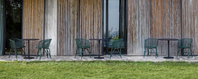 Green chairs and black tables arranged outside against a wooden wall.