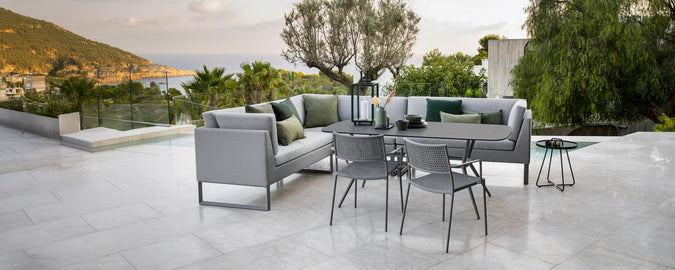 Modern outdoor lounge area with grey sofa, green cushions, black table, and grey chairs.