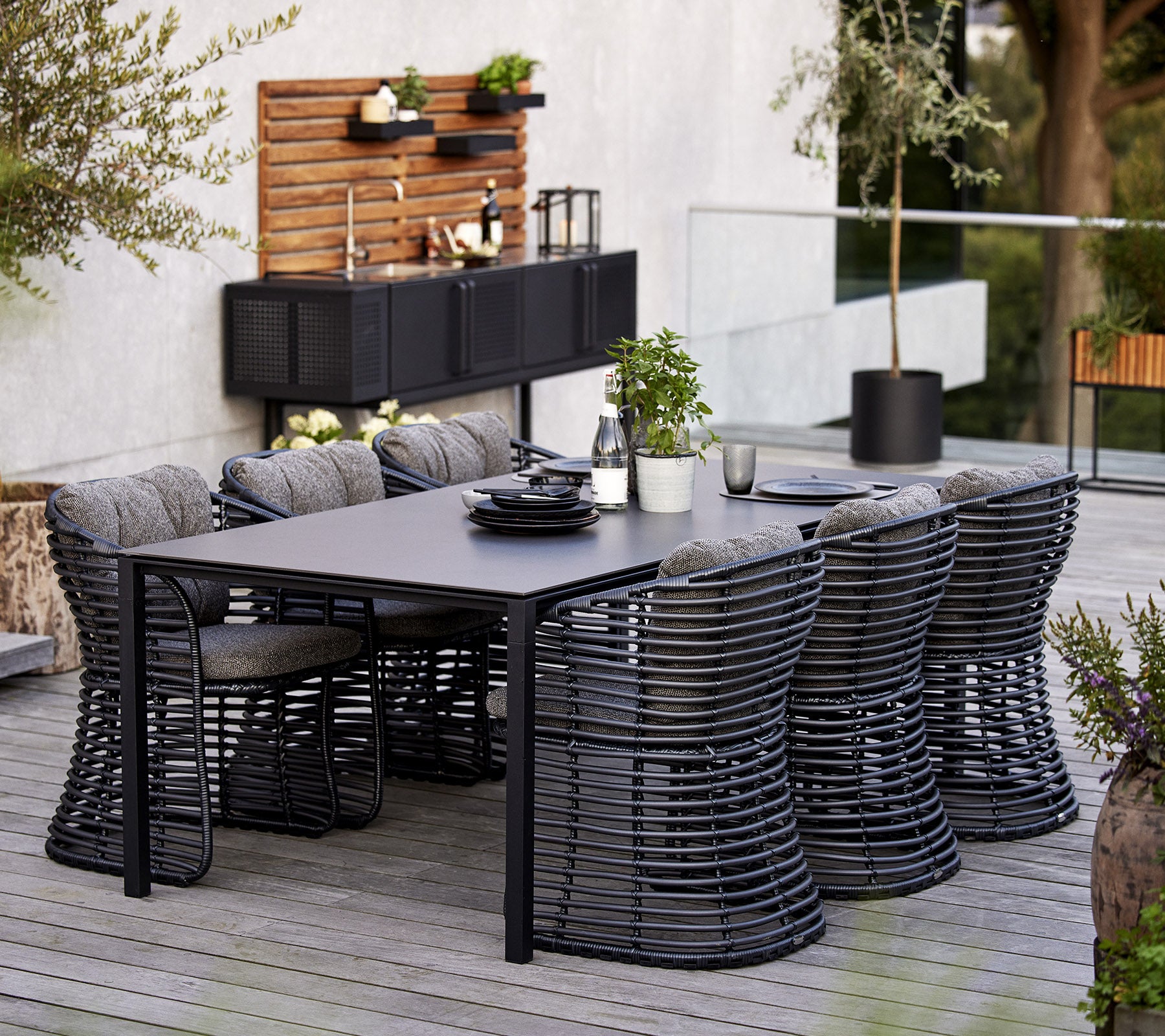 A modern dining set featuring a rectangular table and six stylish basket chairs, complemented by decorative elements in the background.