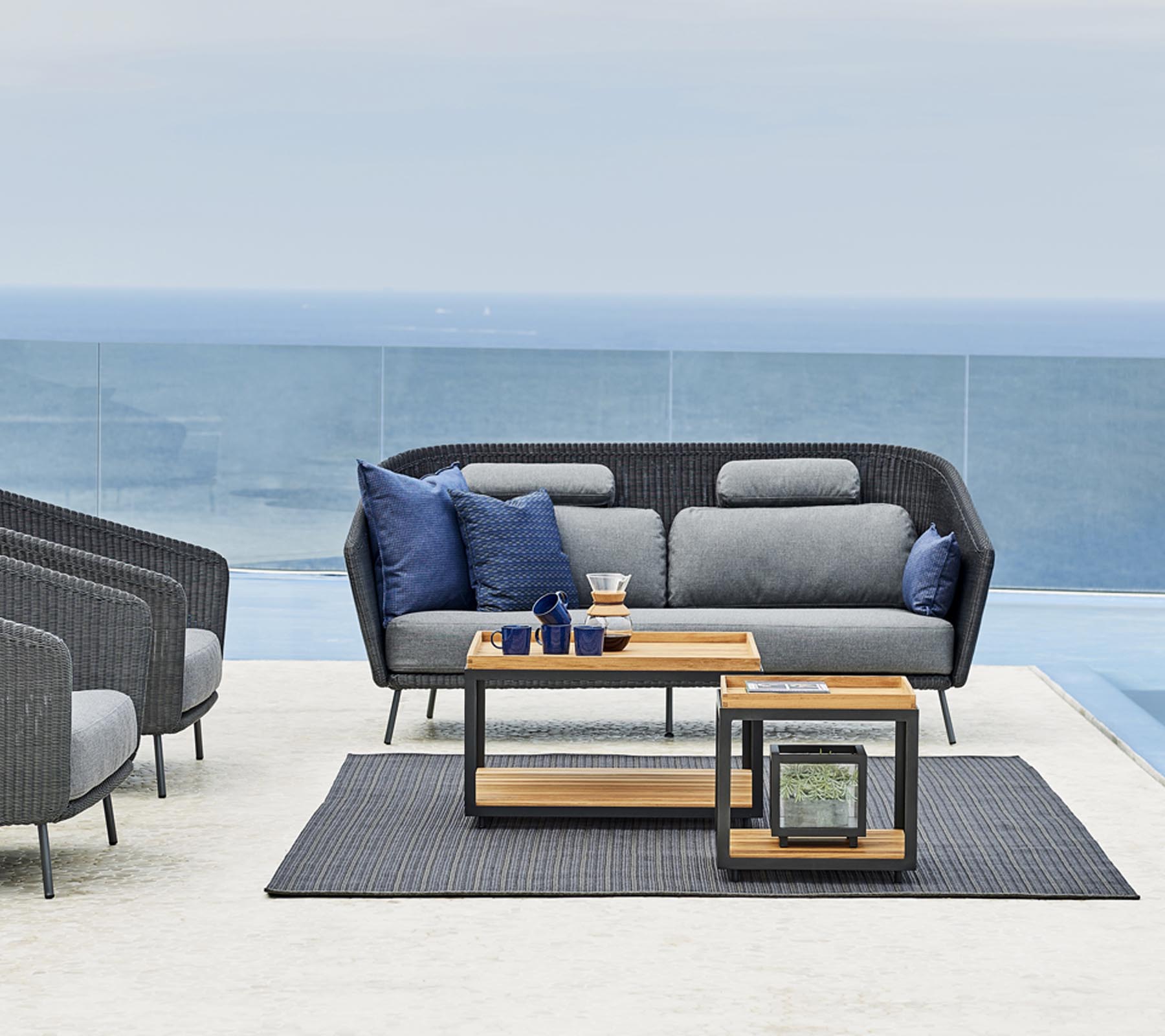 Stylish outdoor seating arrangement featuring a gray sofa with blue cushions, a wooden side table, and a matching rug.