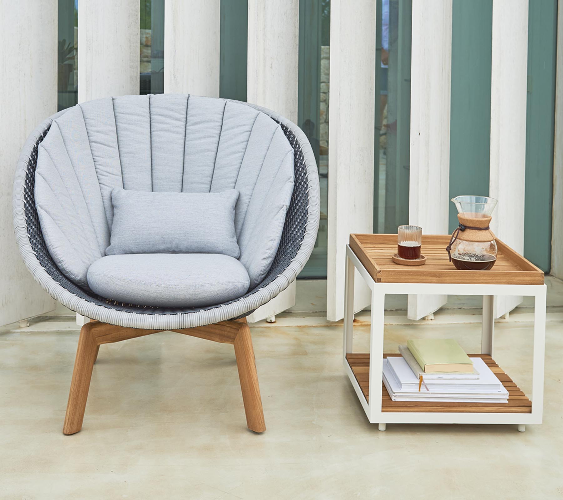 Cozy round chair with plush cushions alongside a neat side table holding beverages and books.