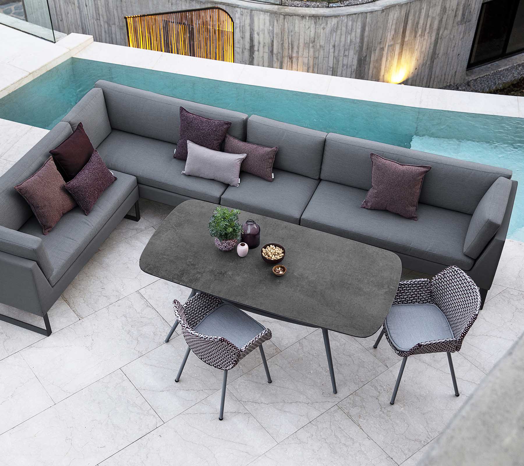 Modern outdoor seating arrangement with a gray sectional sofa, decorative pillows, and a sleek dining table surrounded by stylish chairs.