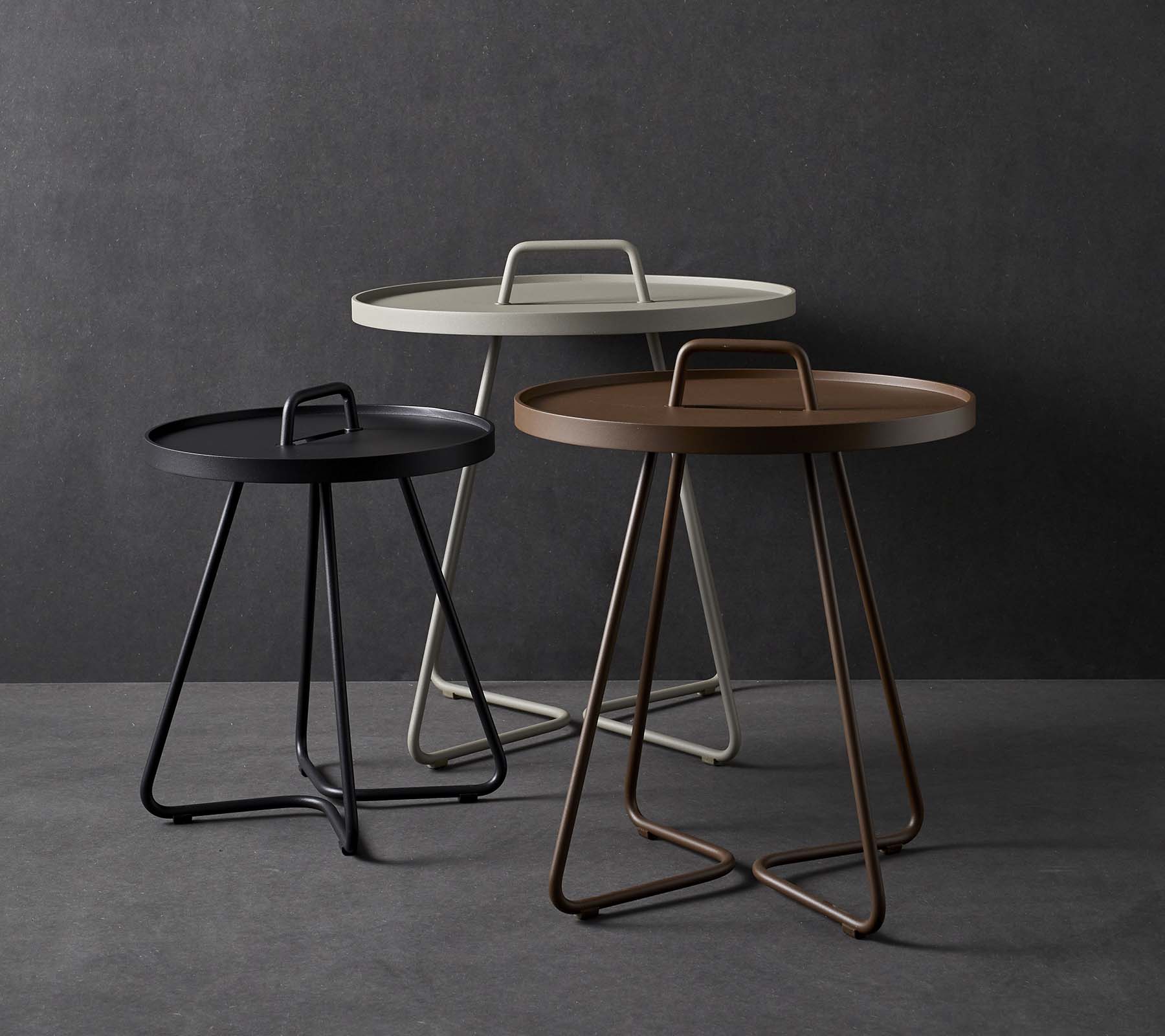 Three stylish side tables with circular tops and unique handle designs, featuring a mix of colors including black, white, and brown.