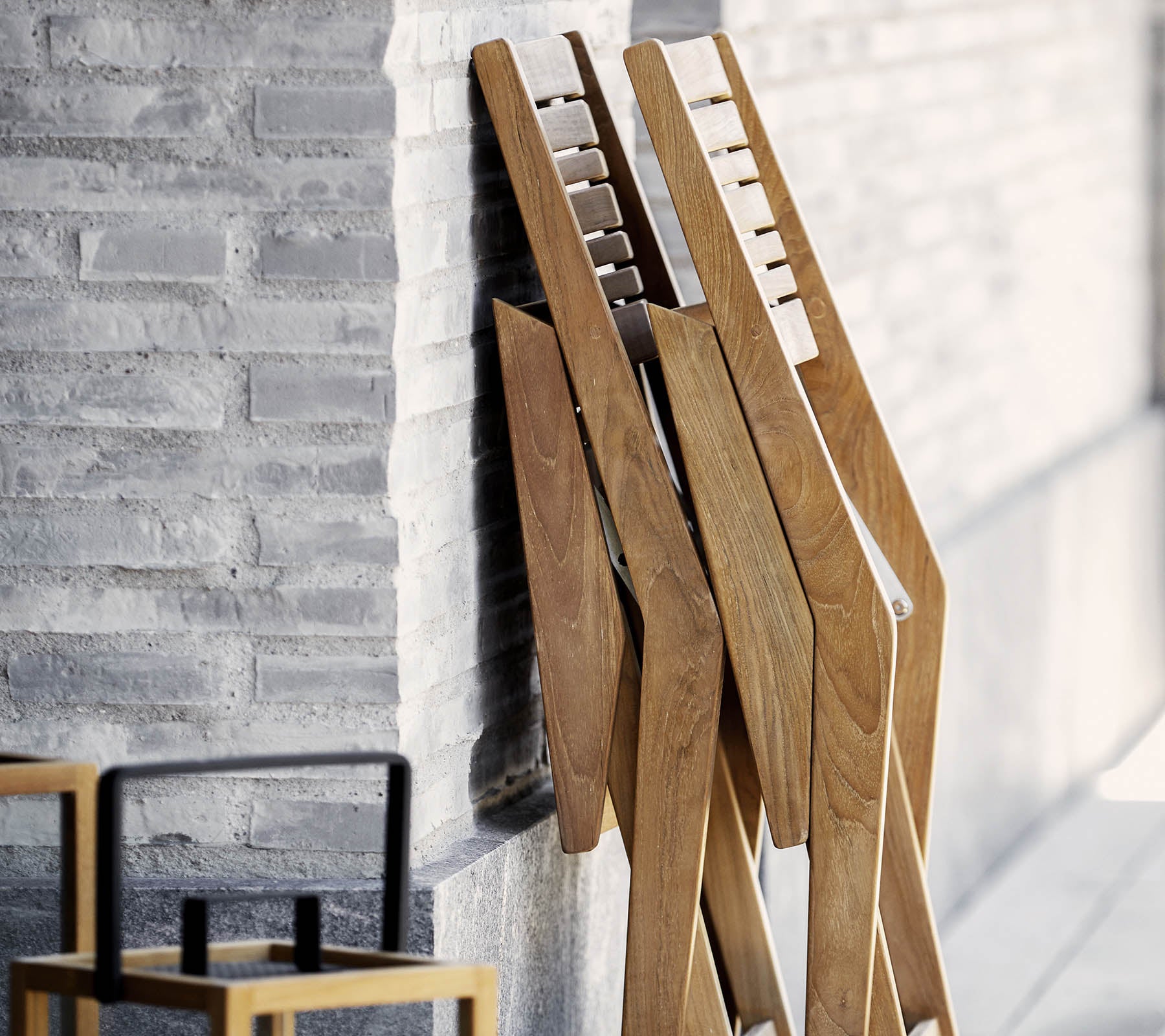Three wooden stands with a sleek design, leaning against a textured wall, accompanied by a simple, stylish chair in the foreground.