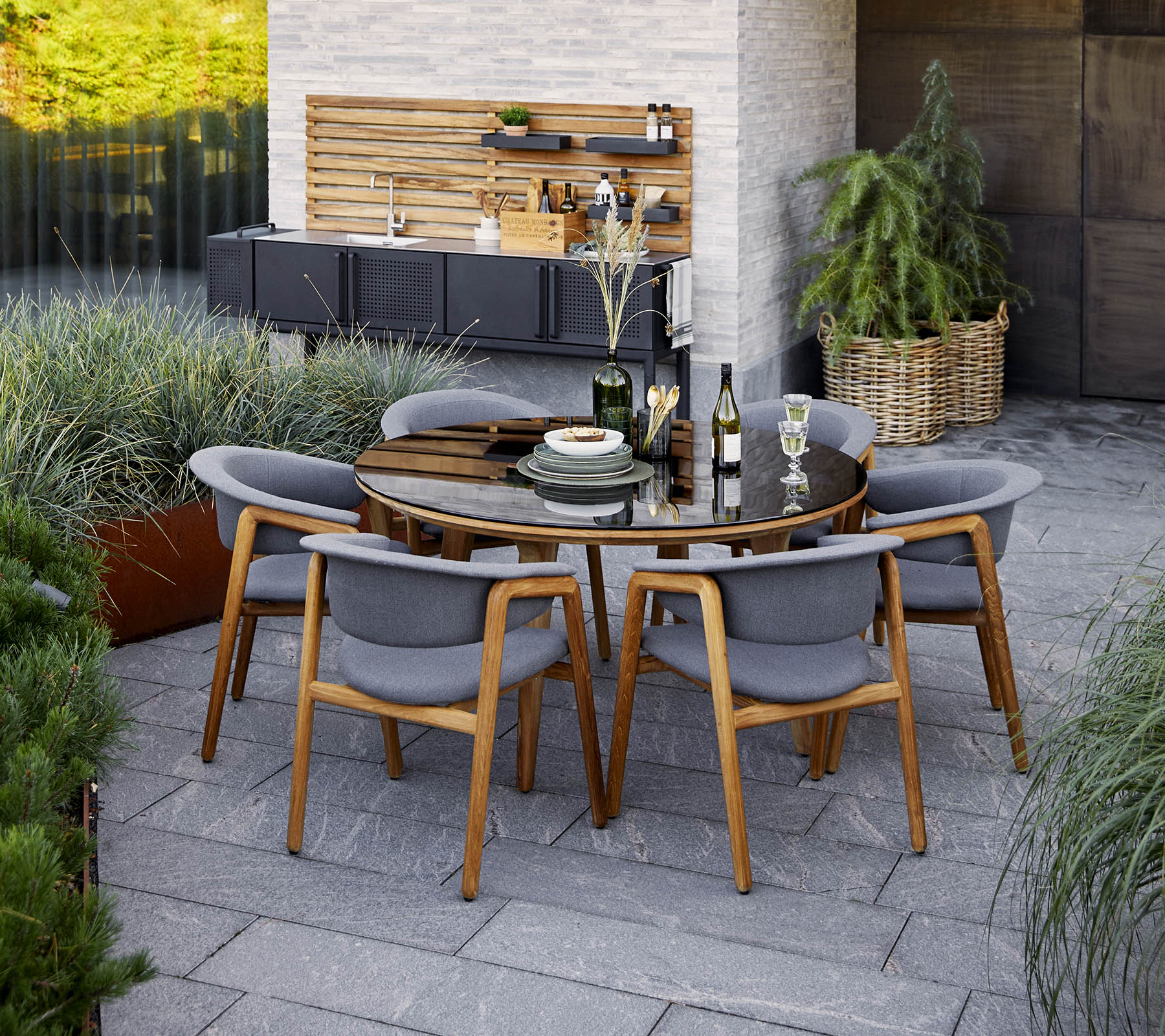 A modern round dining table set with gray chairs, featuring decorative elements and greenery in the background.
