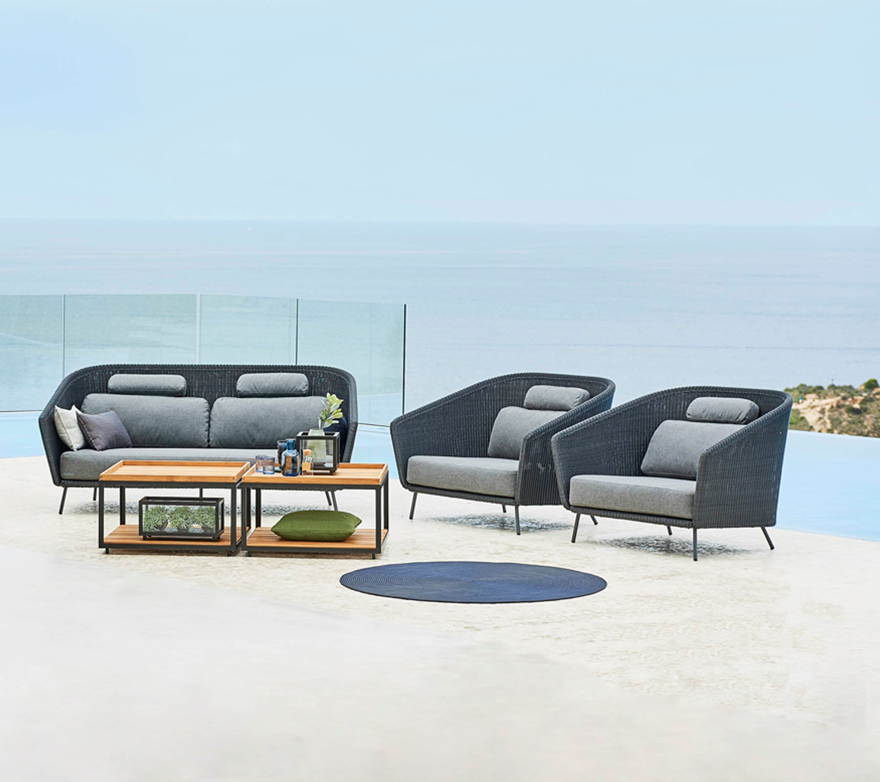 Stylish outdoor seating arrangement featuring a sofa and two chairs, complemented by a coffee table and decorative elements, with a scenic backdrop.