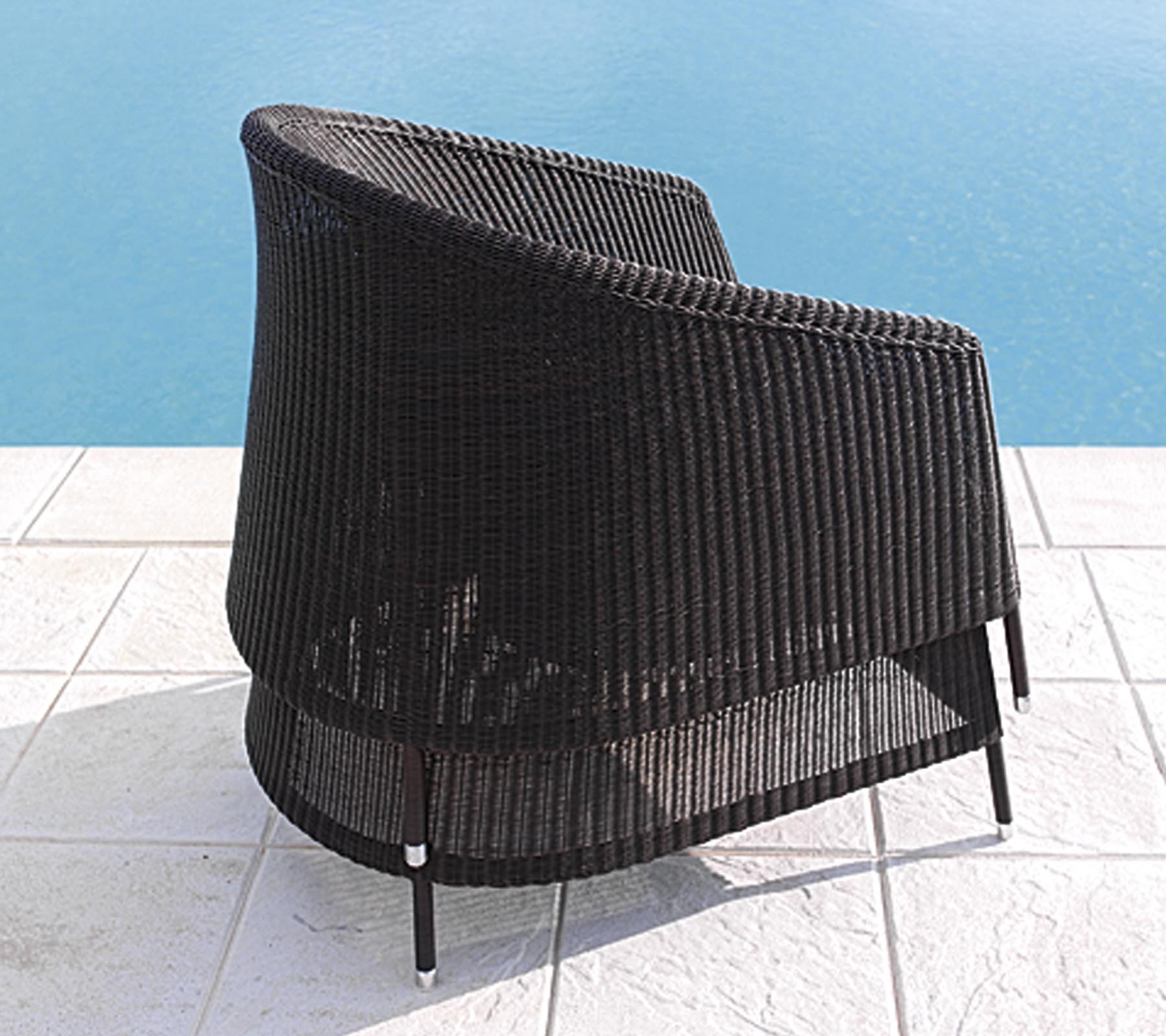 Curved black wicker chair with a sleek design, positioned near a pool on white tiled flooring.