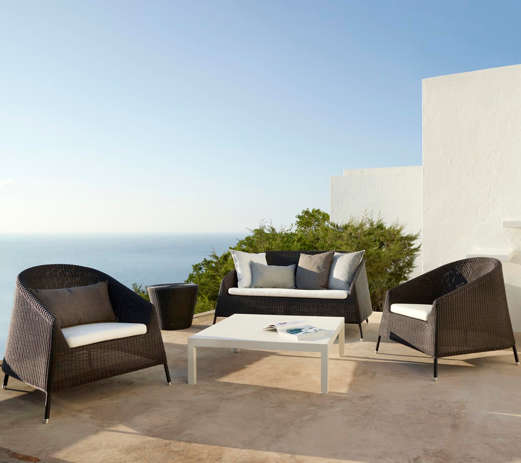 Stylish outdoor seating arrangement featuring a sofa and chairs with cushions, complemented by a glass-top table, ideal for relaxation.
