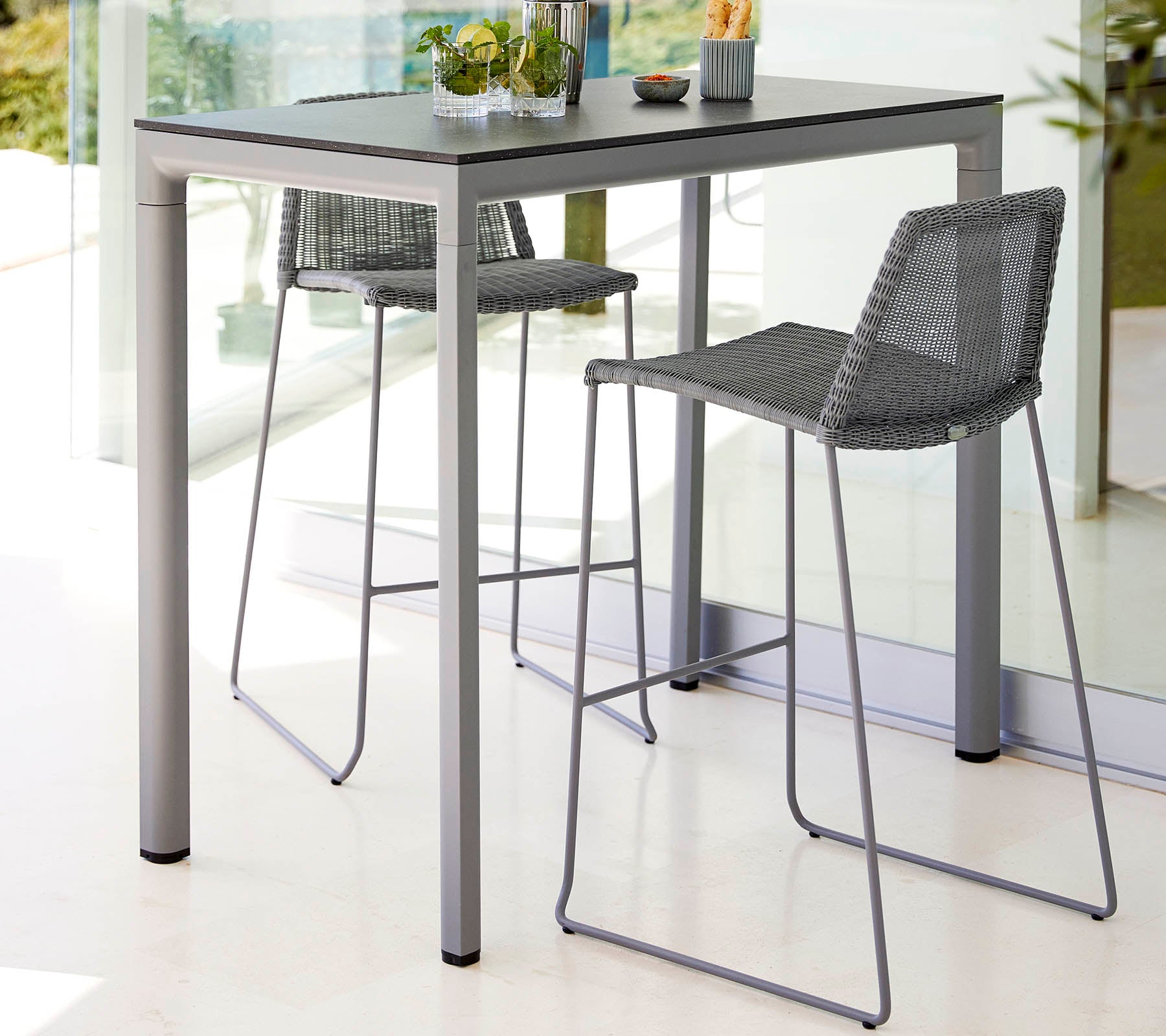 A sleek table with two high stools, featuring a modern design and light color scheme, complemented by a small plant centerpiece.