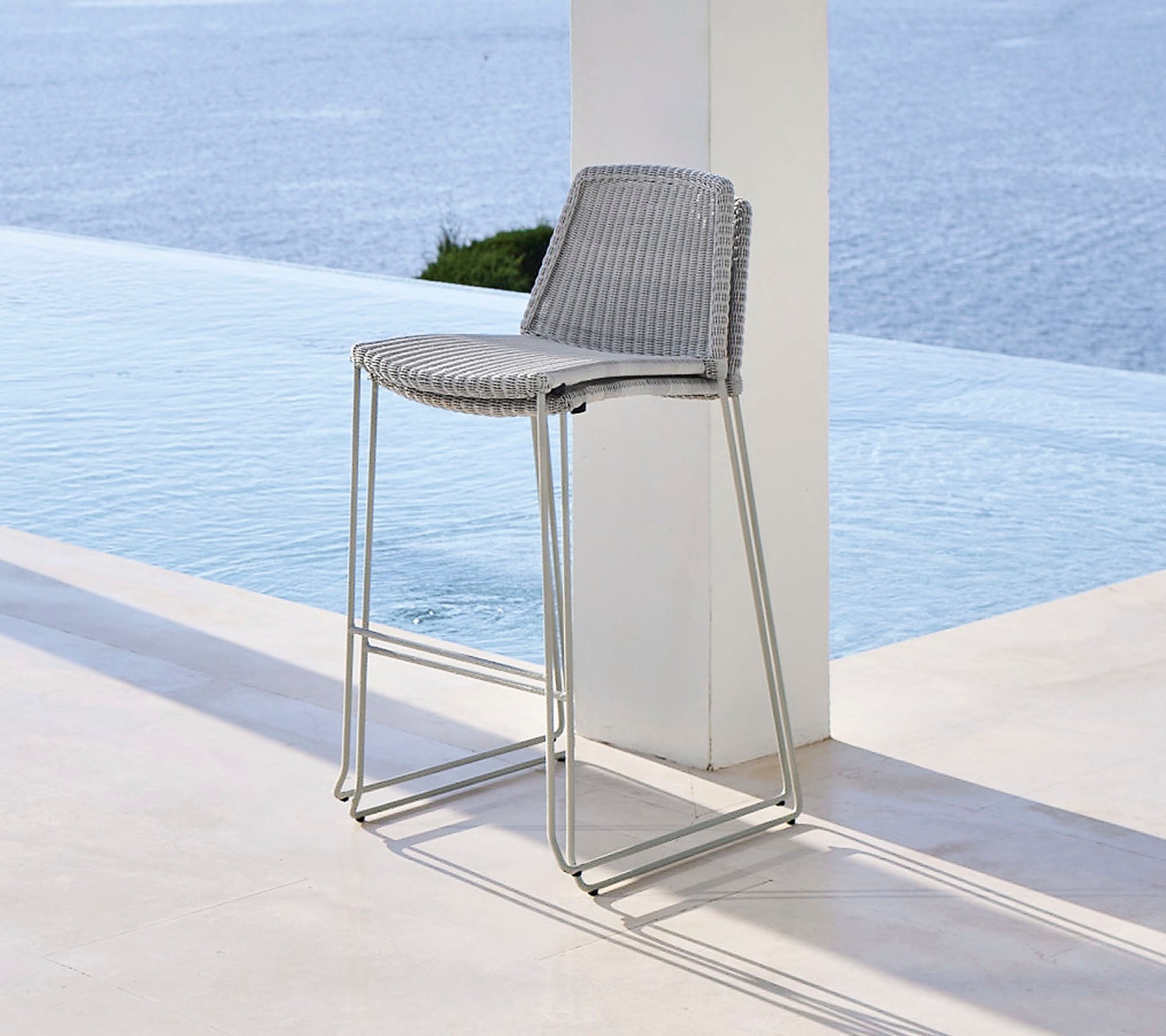 Stylish bar stool with a woven seat and sleek metallic legs, positioned near a tranquil water feature.