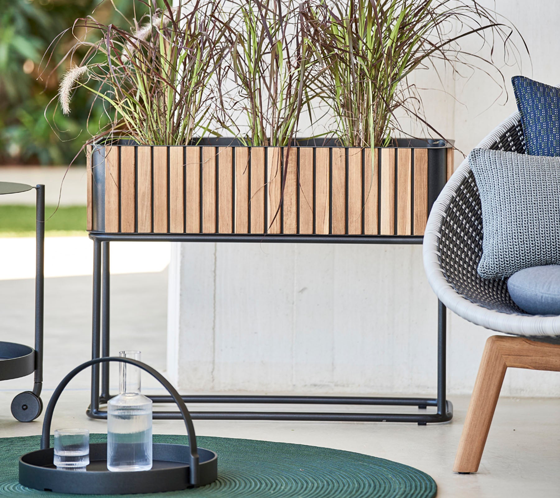 Wooden planter box with decorative plants, accompanied by a round tray holding glasses and a modern chair with soft cushions.