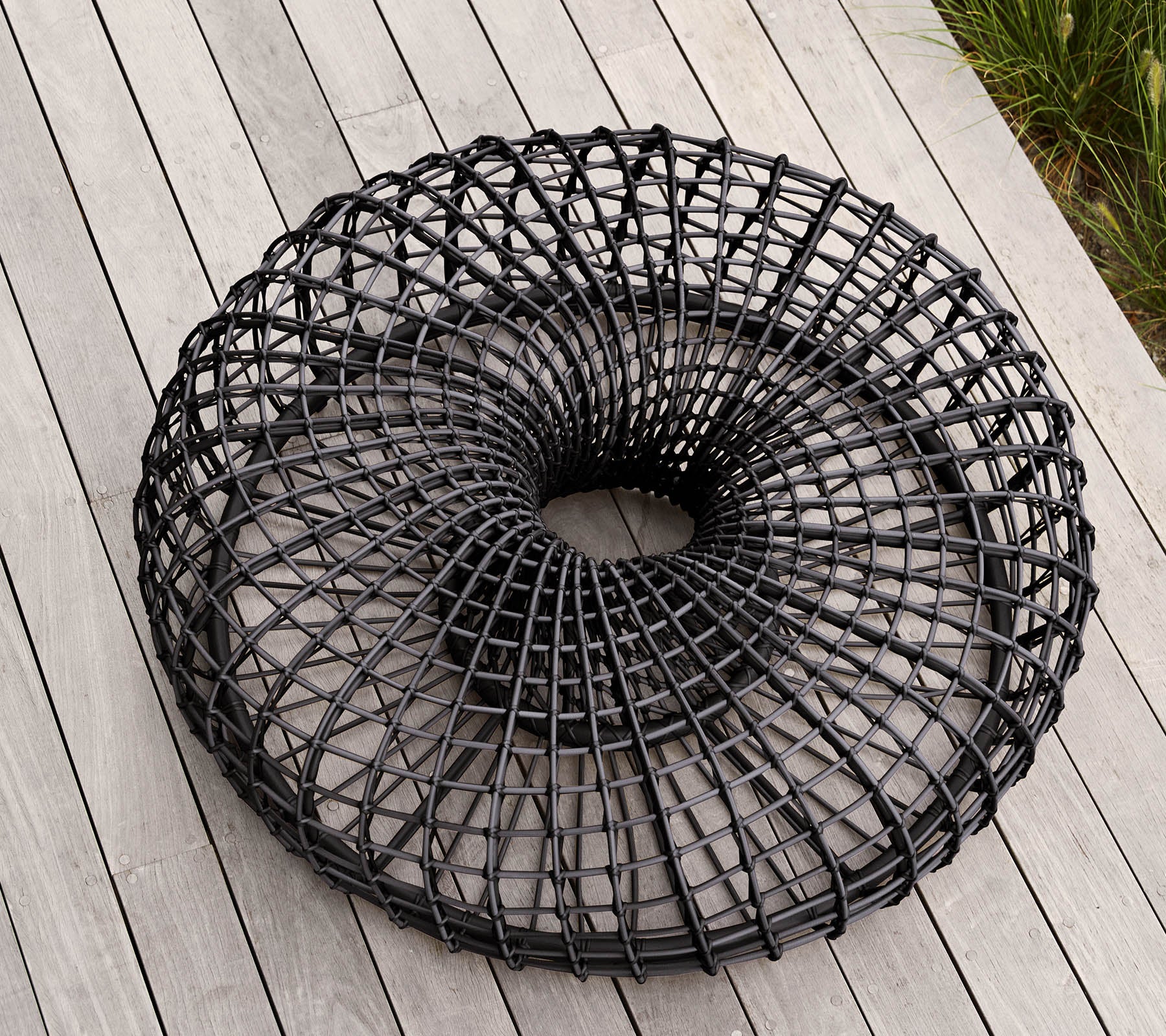 Modern, circular black wire basket with a unique open weave design, resting on a flat surface. Ideal for storage or decorative purposes.