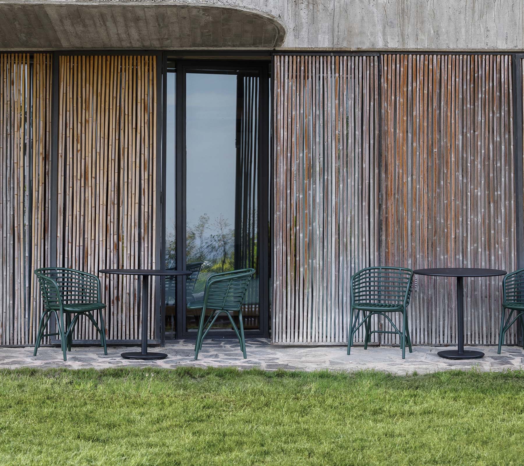Chairs and tables arranged in front of a wooden panel backdrop, complemented by a grassy area.
