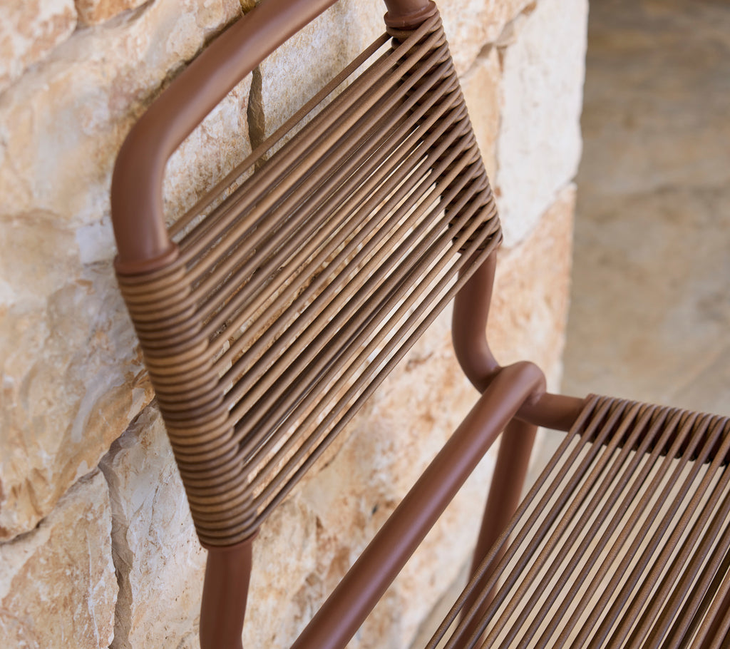 Brown chair with a slatted design against a stone wall.