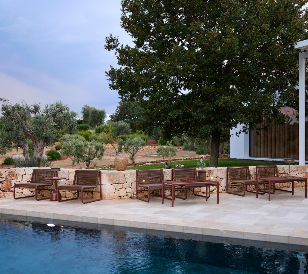 Brown chairs arranged by a pool with a landscaped background.