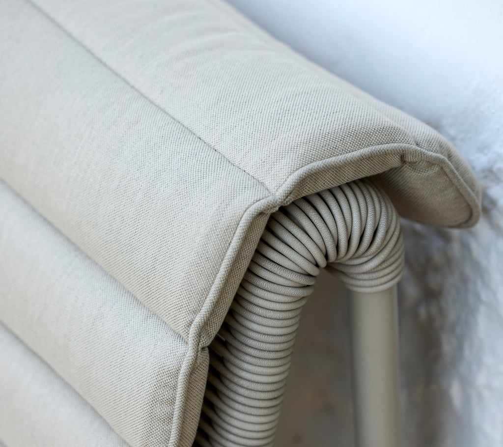 Beige cushion with a ribbed texture resting against a light wall.