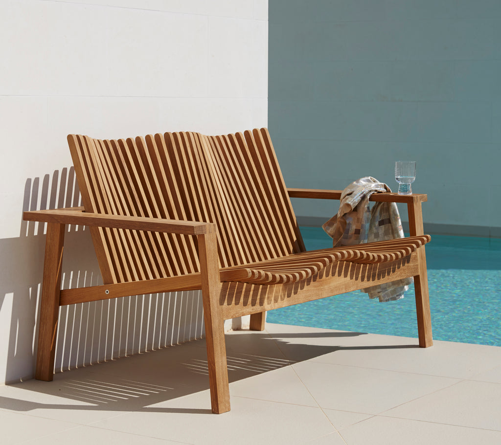 Side view of a sleek, wooden 2-seater sofa with slatted design, accompanied by a drink and a towel. Ideal for relaxed seating.