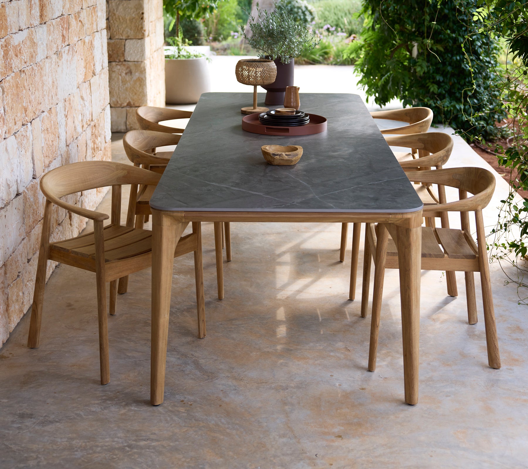 Modern outdoor dining table with black surface and wooden chairs in a natural setting.