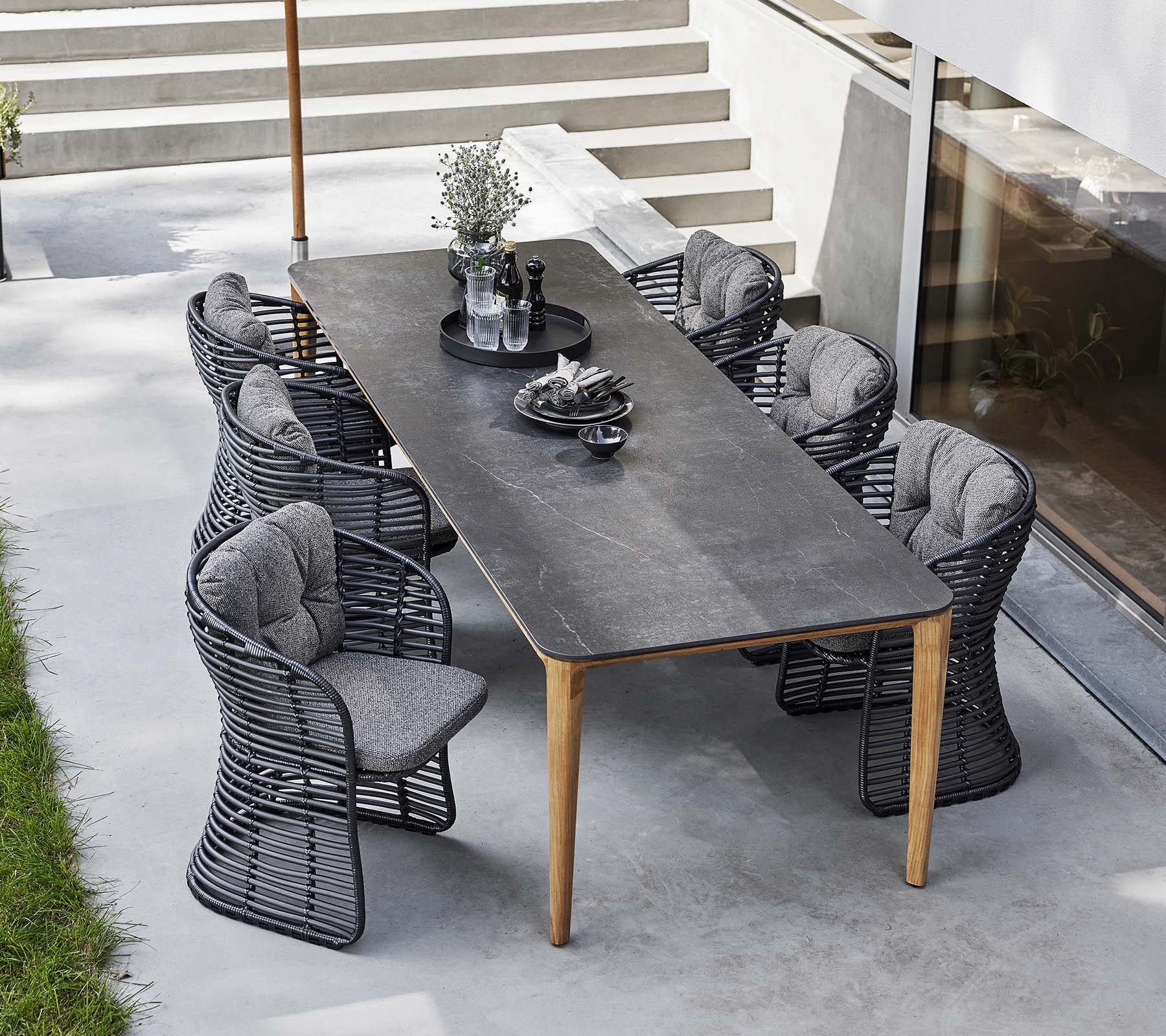 Basket chairs surround a sleek table, complemented by a classic parasol and decorative centerpieces for an inviting outdoor dining setup.