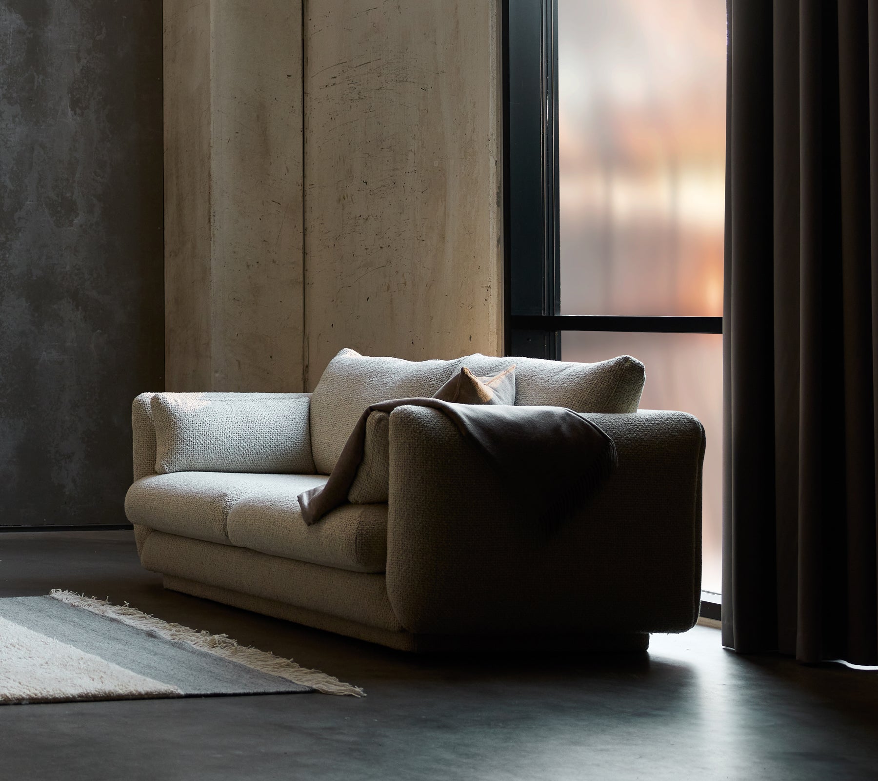 Bloom 2-seater sofa in sand flair, featuring a plinth design and a cozy throw draped over one side.