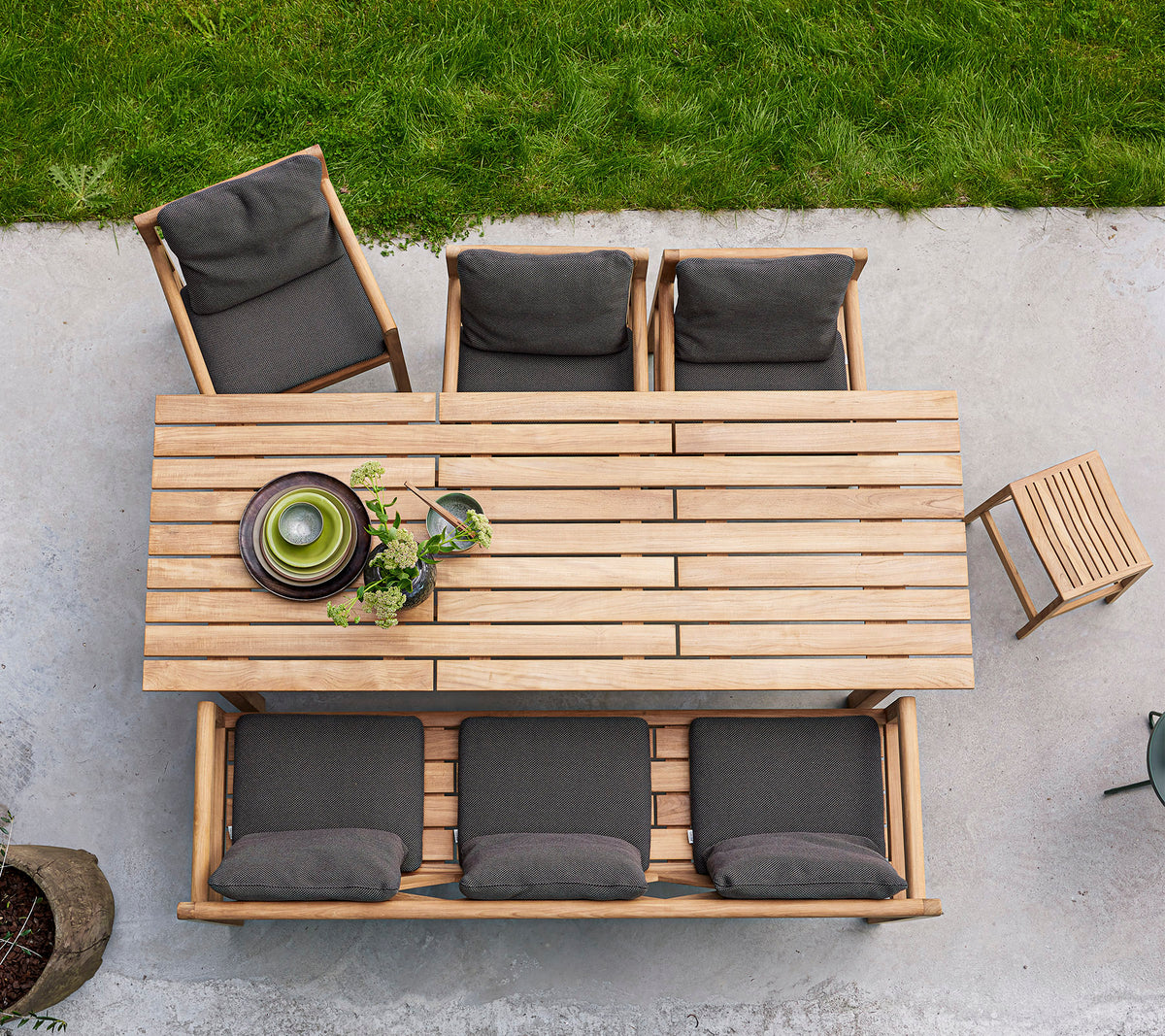 A wooden dining table with four cushioned chairs and a bowl of greenery, arranged for an inviting gathering.