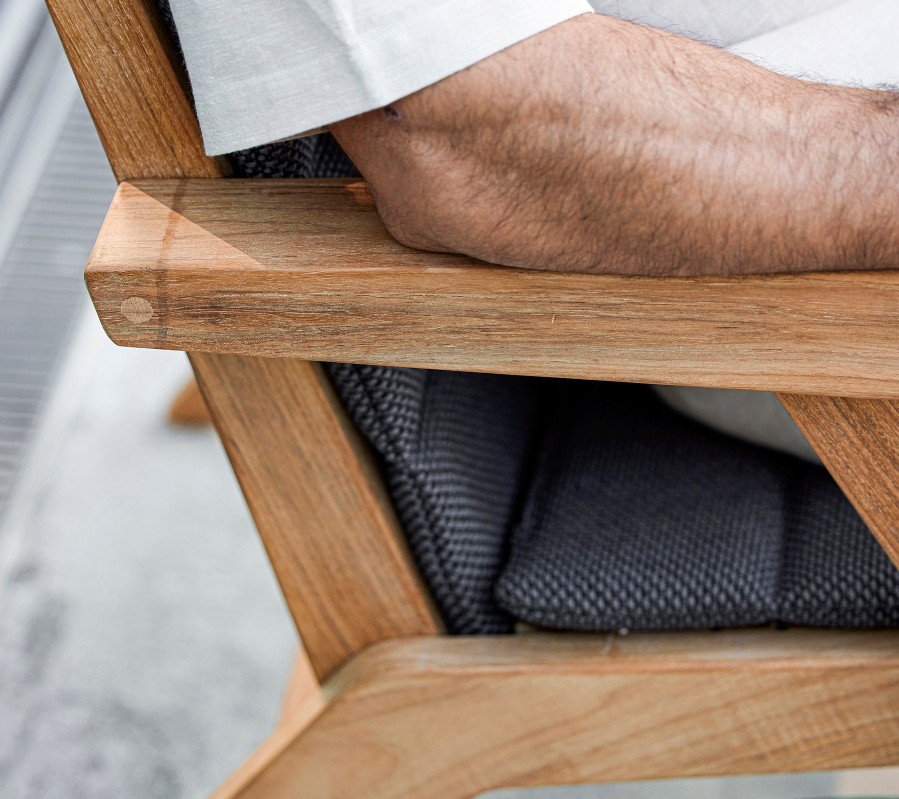A close-up of a wooden chair arm with a padded seat, featuring an arm resting on it, showcasing a blend of natural and textured materials.