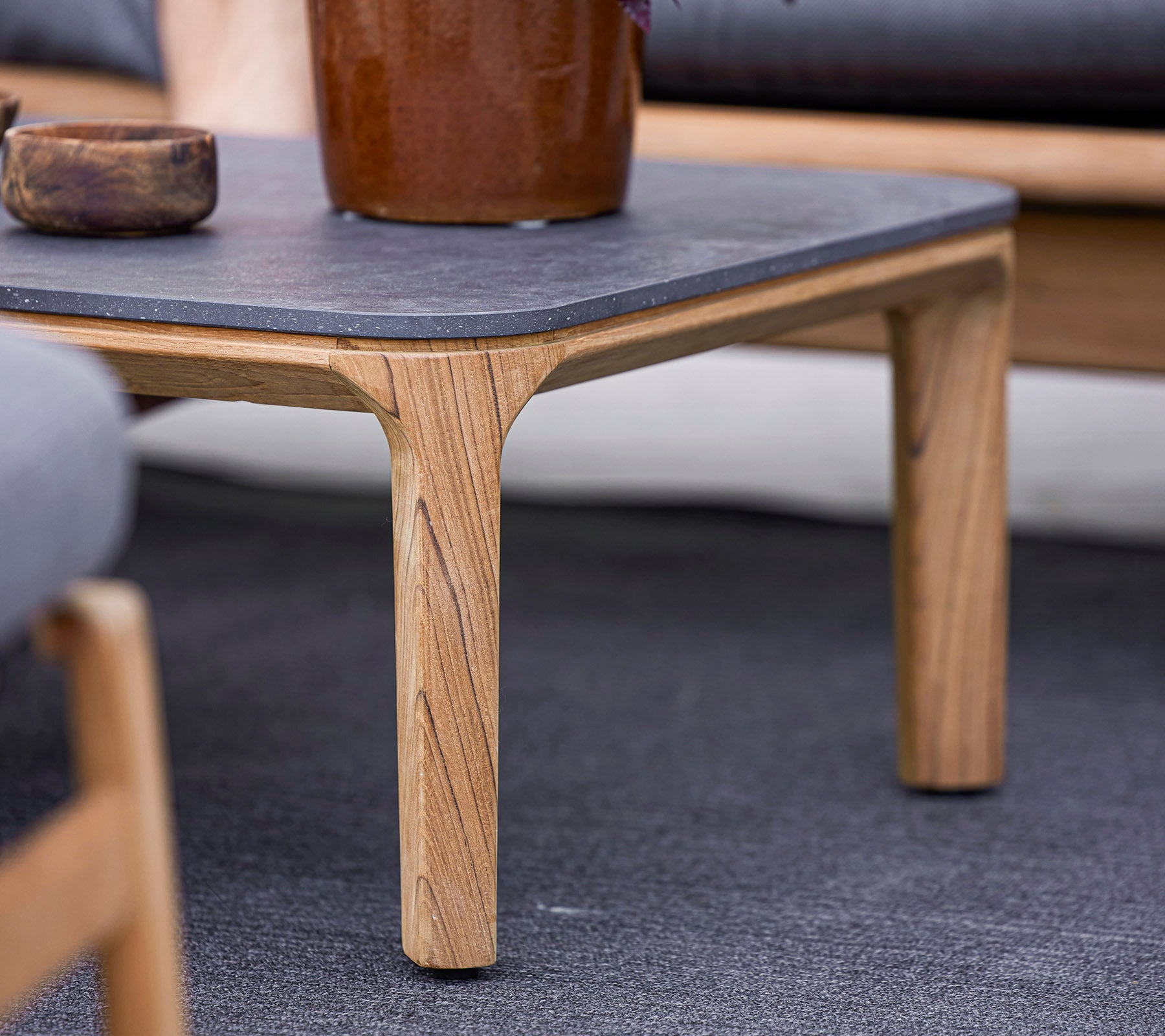 A wooden table with a dark stone top, featuring uniquely carved legs, surrounded by soft seating and a decorative plant pot.