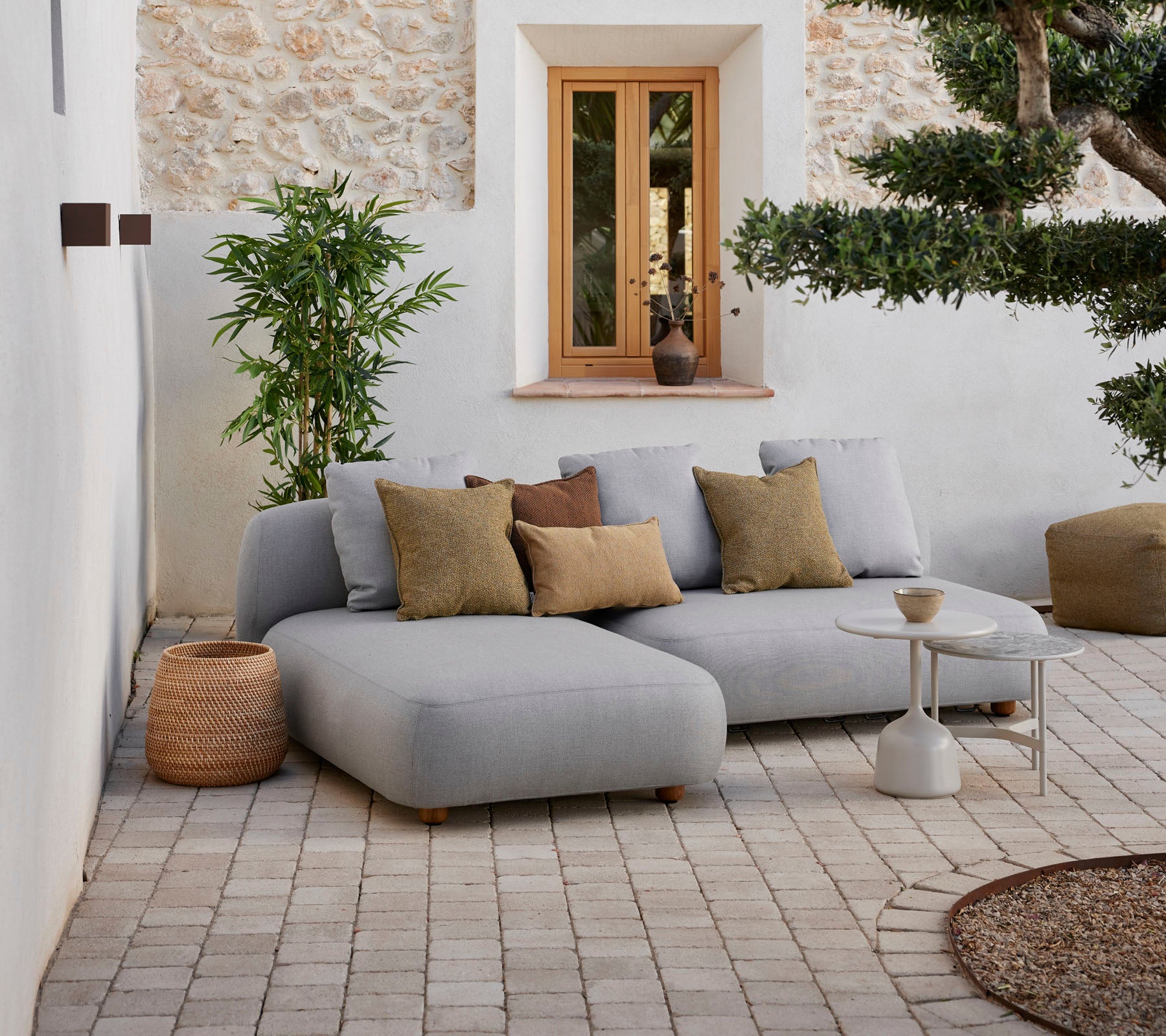 Modern gray sectional sofa with decorative cushions, small side table, and natural elements in a cozy setting.