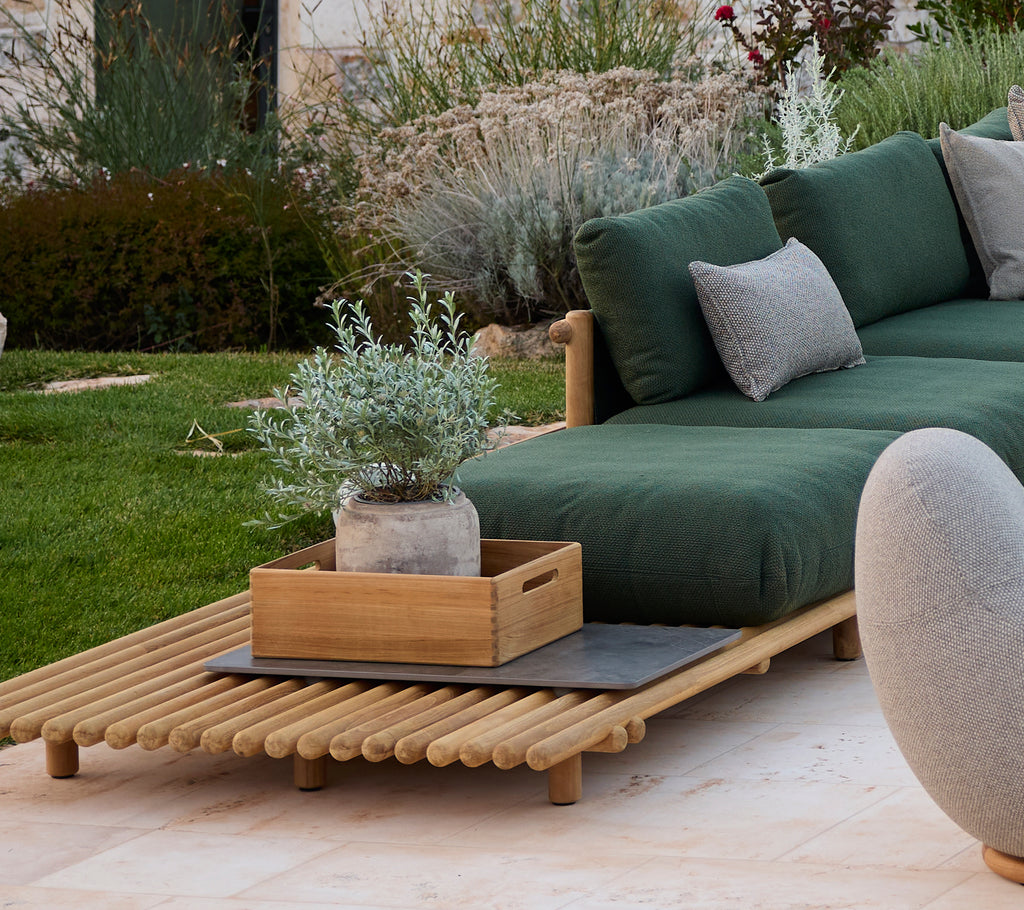 Modern outdoor lounge area with sofa, green cushions, wooden coffee table, and potted plant.