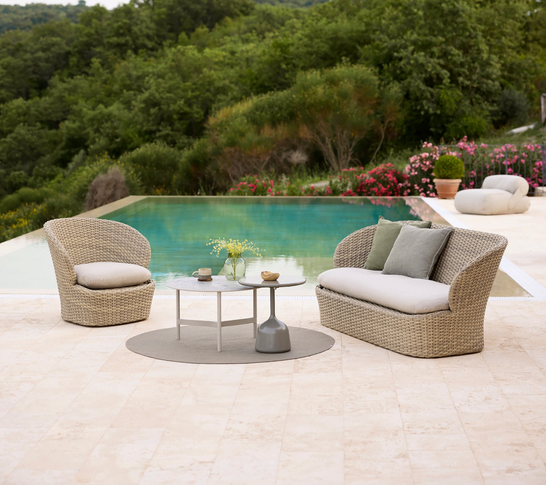 Coastal lounge seating with soft cushions, paired with a Twist coffee table and a Glaze coffee table, surrounded by lush greenery and a pool.