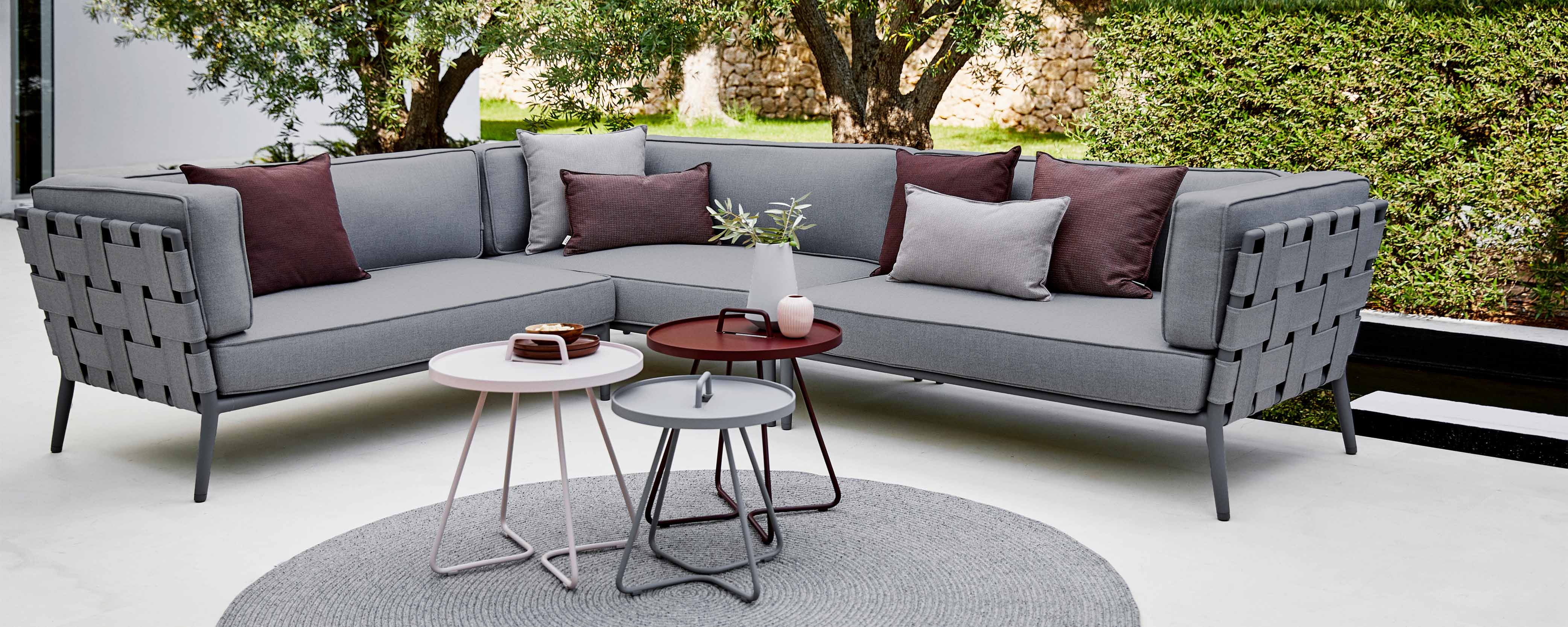Modern conic sectional sofa in gray fabric with decorative cushions, accompanied by stylish side tables and a round rug.