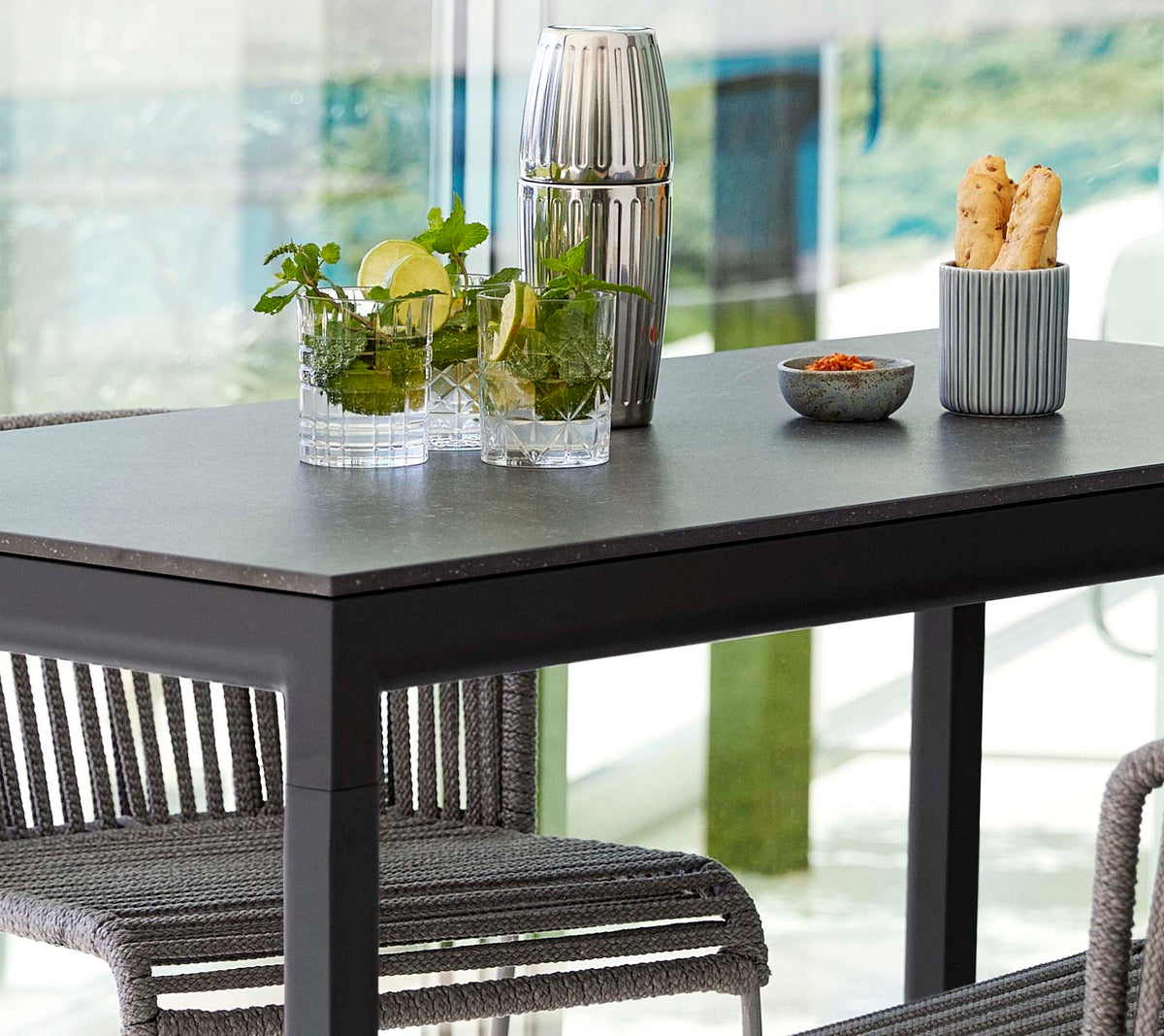 A modern table set with plants in glass vases, a decorative container, and a dish of snacks, surrounded by stylish chairs.