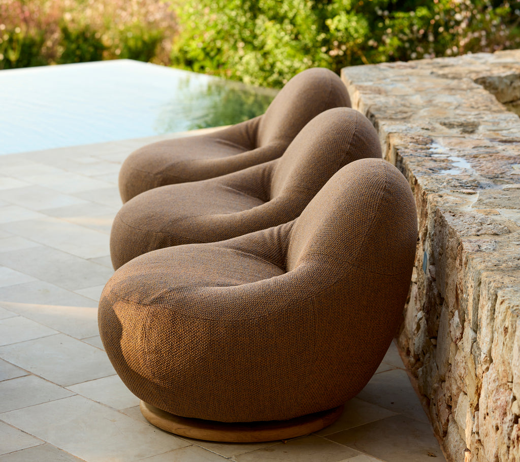 Set of three modern brown chairs arranged near a stone wall.