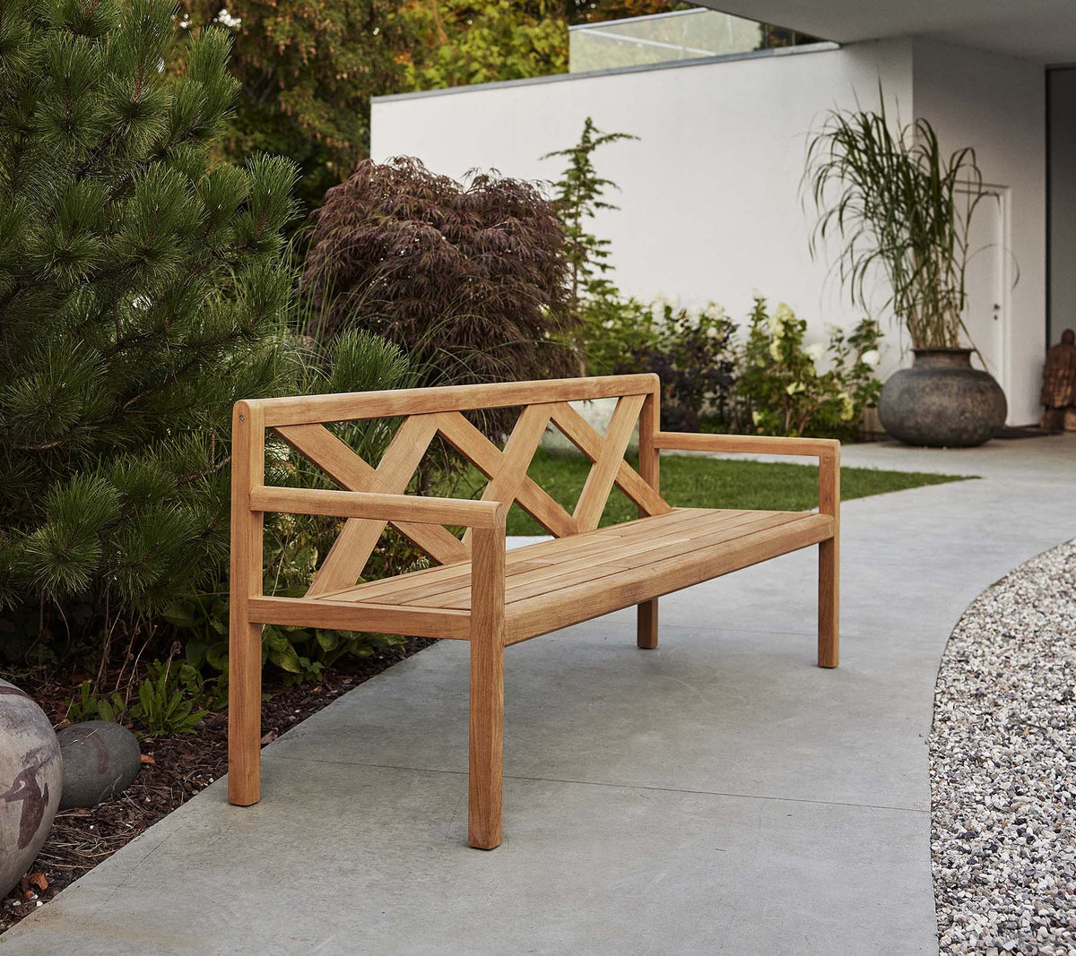 A sleek wooden bench featuring a decorative backrest, surrounded by greenery and decorative elements, perfect for outdoor relaxation.