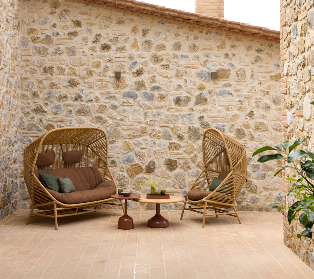 A cozy seating area featuring Hive rocking chairs and a Hive sofa, complemented by Glaze coffee tables and a stone wall backdrop.