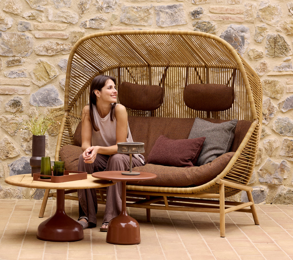 A woman relaxes on a Hive sofa with cushions, accompanied by Glaze coffee tables and a club tray, against a stone wall backdrop.