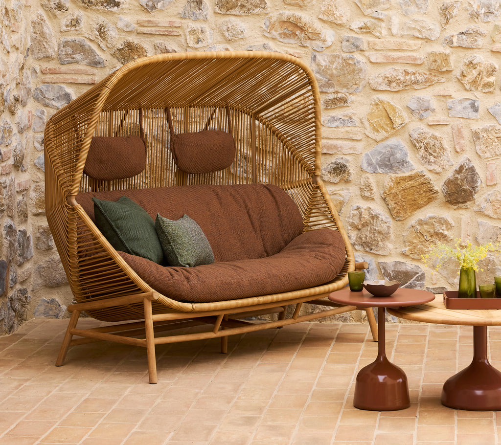 A stylish rattan sofa with brown cushions and green scatter cushions, accompanied by two contemporary coffee tables.