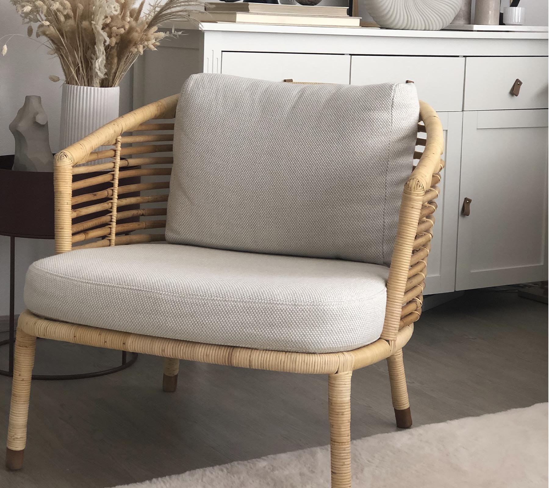 A stylish chair with a woven design and soft cushions, paired with a decorative plant and stylish storage unit in the background.