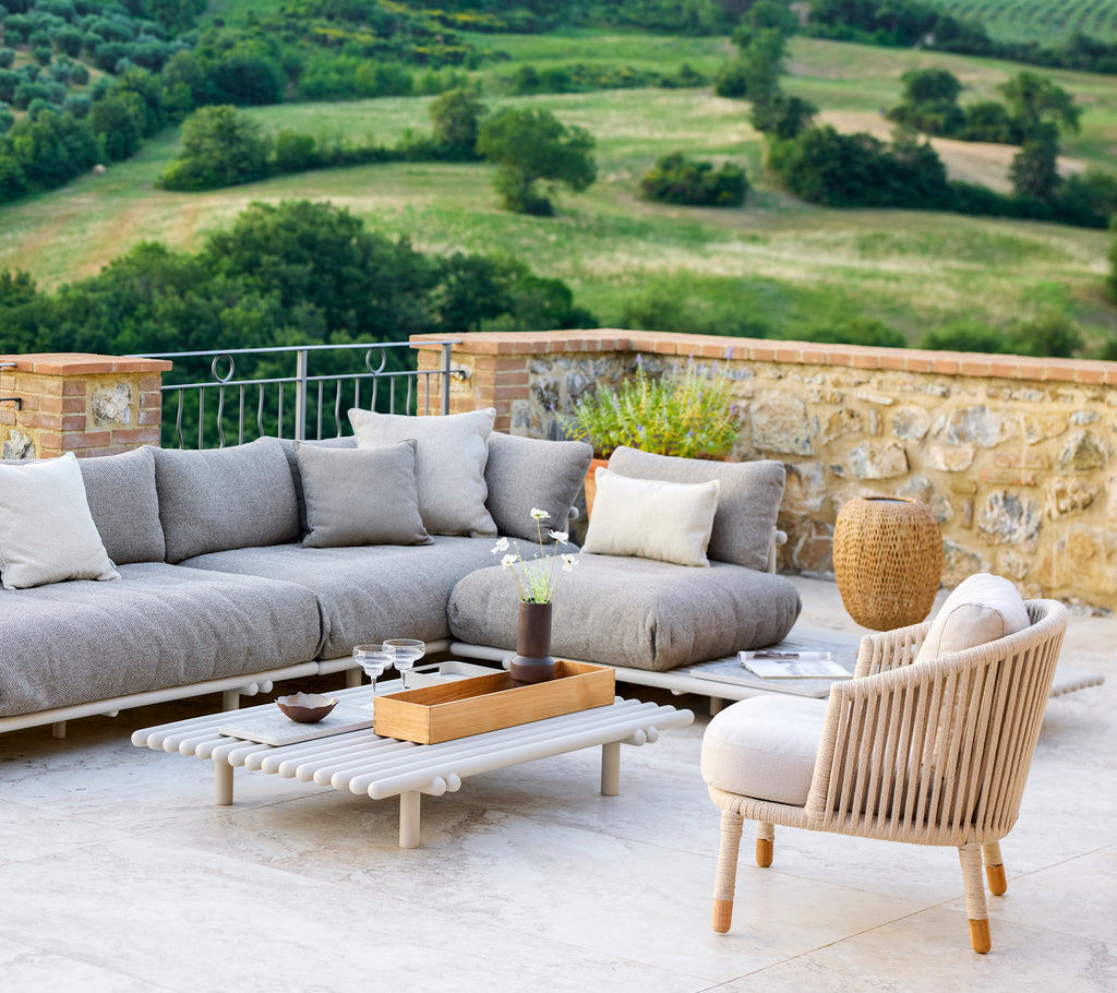 Stylish lounge setup featuring a cozy sectional sofa, a light accent chair, and modern decor against a serene landscape backdrop.