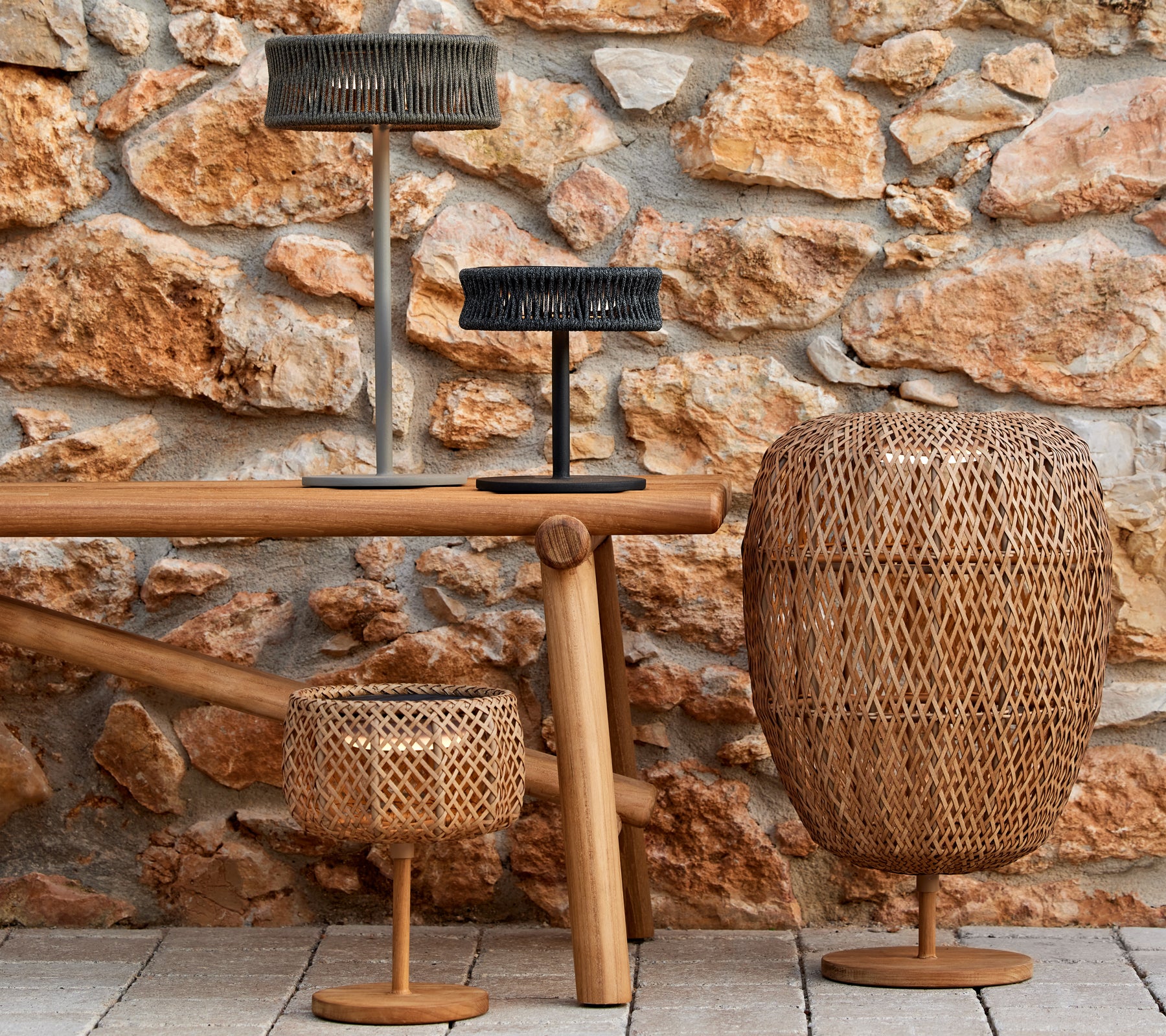 A trio of stylish woven lamps in varying sizes, highlighting the interplay of light and texture against a rustic stone backdrop.