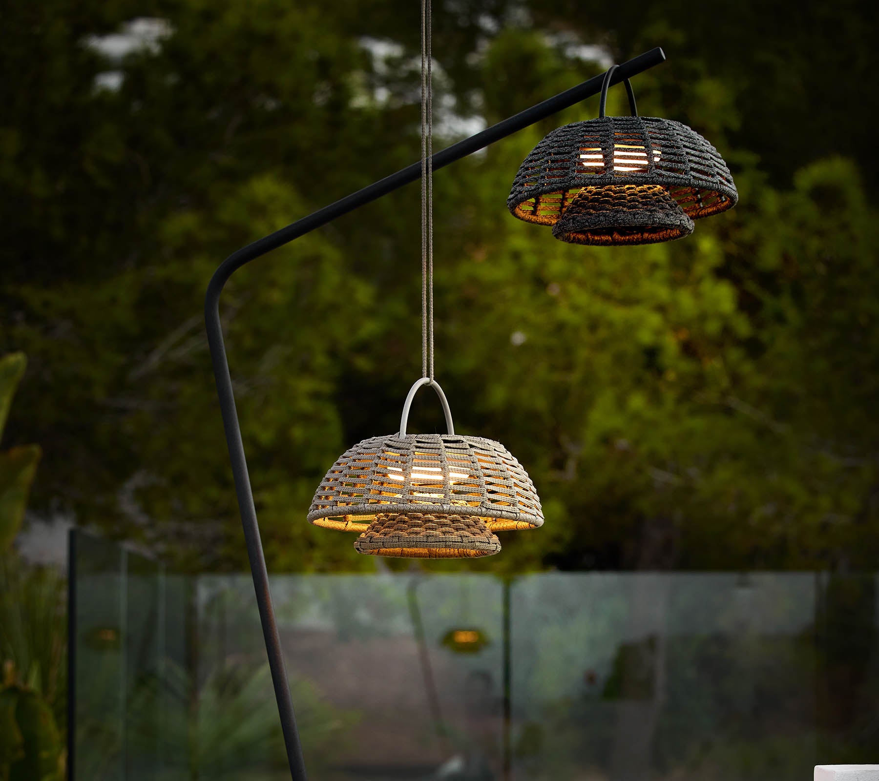 Two illusion lamps with woven designs, suspended from a sleek black stand, casting warm light against a dark backdrop.