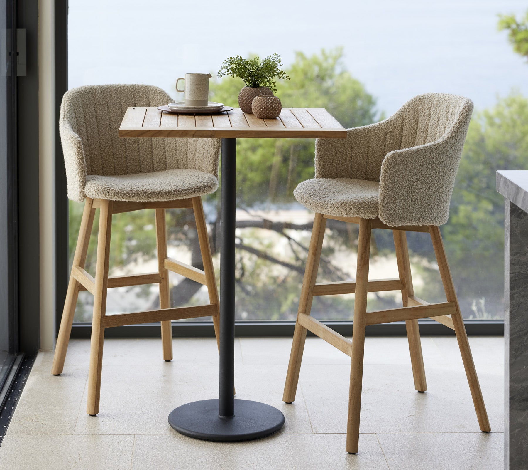 A small table with two upholstered chairs, a cup, and decorative items, set against a natural backdrop.