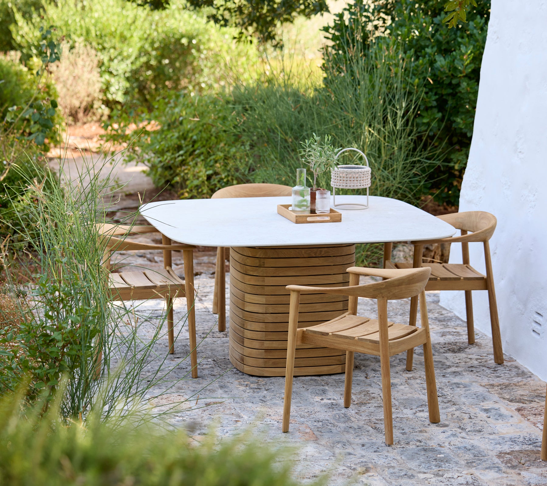 Modern outdoor setting featuring a white table and wooden chairs surrounded by greenery.
