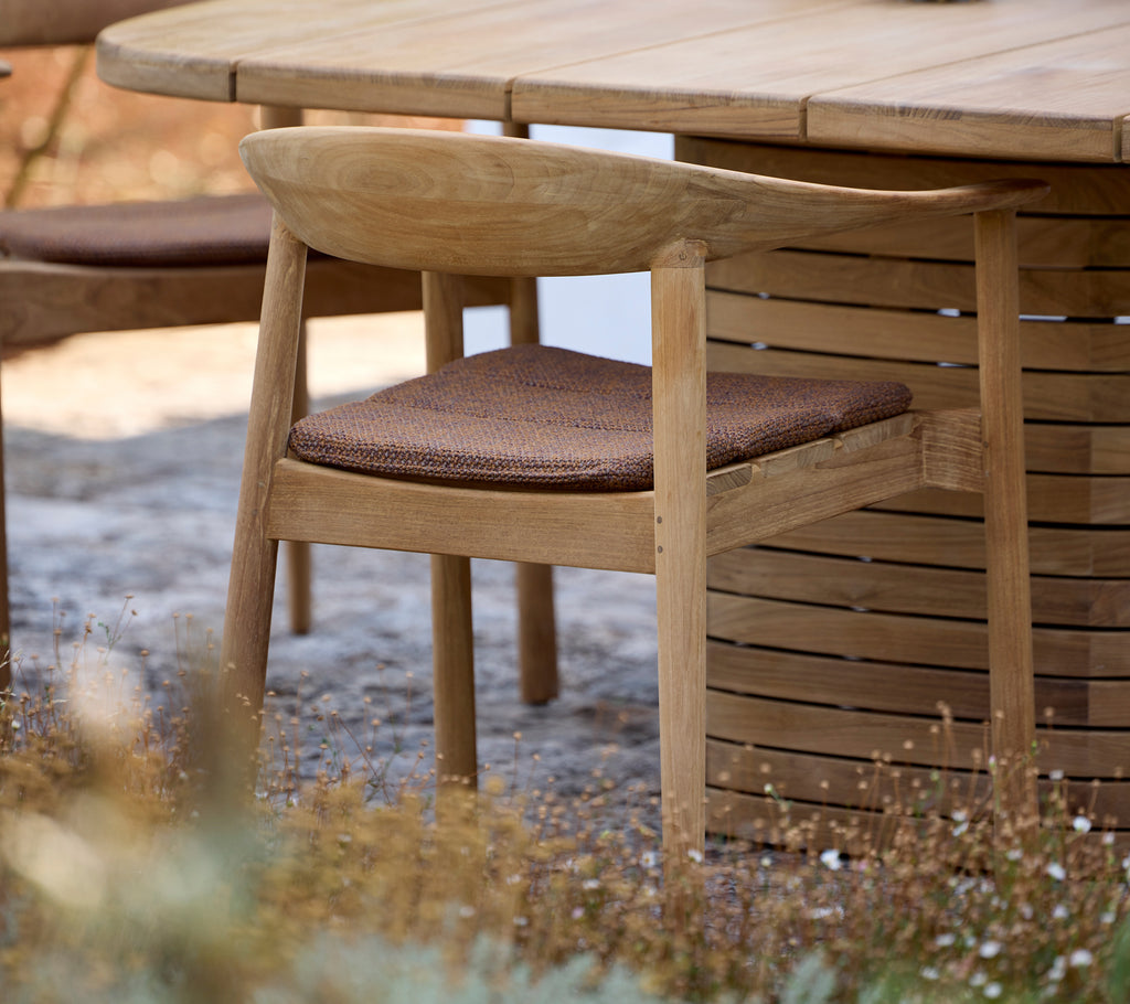 Wooden chair with brown cushion beside a round table in an outdoor setting.